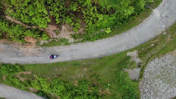 Aerial View of a Motorcycle with a Man Riding Along a Curved Road in the Mountains Around a Green