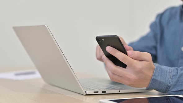 Close Up of Man Using Smartphone with Laptop