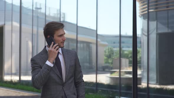 Young Businessman in a Suit Standing Near a Glass Skyscraper and Talking on a Mobile Phone, Top