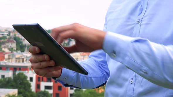 Young Handsome Business Man Works on Tablet - City (Buildings) in Background - Closeup