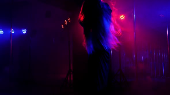 A Young Woman is Dancing on a Pole in a Dark with Bright Multicolored Spotlights