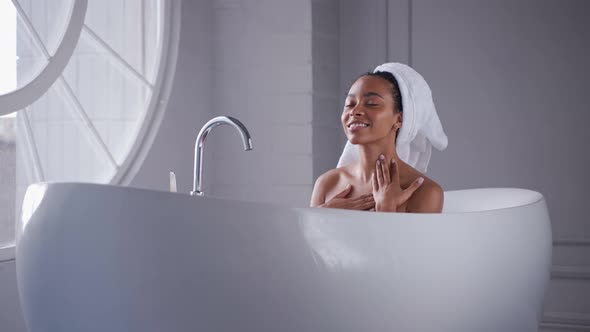 Black Woman Taking a Bath Touching Her Neck with Her Hair Wrapped in a Towel