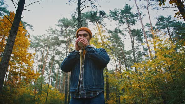 Below View of Male Tourist Enjoying Hot Tea and Calmness of Nature in Autumn Forest Tracking Shot