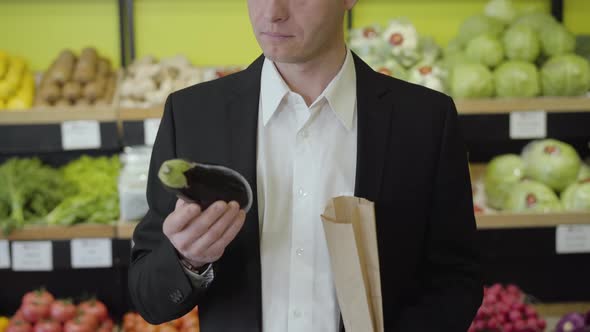 Serious Caucasian Man in Suit Smelling Eggplant, Putting It Into Paper Pack and Leaving. Young