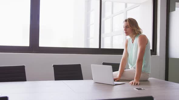 Professional businesswoman with laptop looking out of a window from her modern office in slow motion