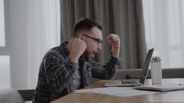 Man Sitting at Home Table Looking at Laptop Screen Feels Pleased with Pride for the Work Done