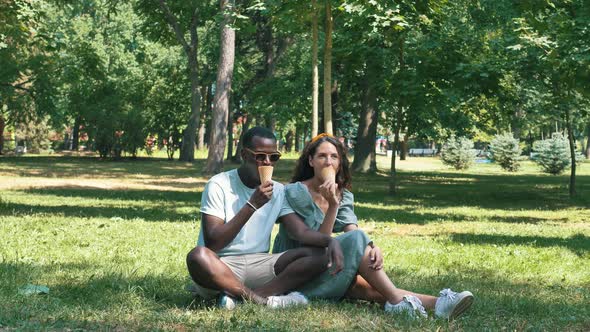 Different Races Couple Sits on Grass Eating Icecream Cones