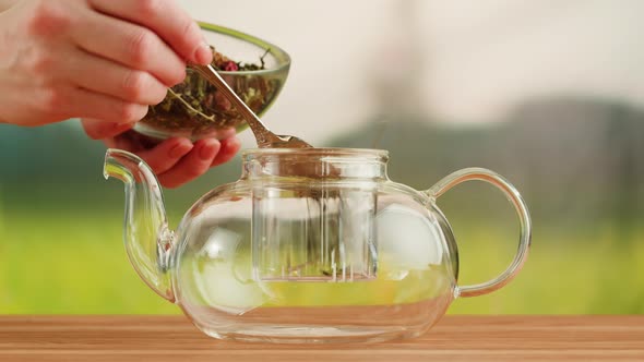 Putting Dry Tea Leaves Into Teapot on a Wooden Table