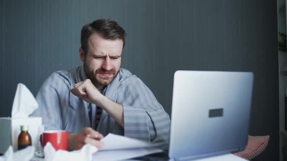 Sick Business Man Working with Laptop Computer and Documents at Home. Man Blowing His Nose