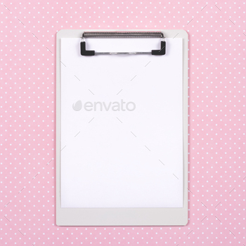 Top view of clipboard with white page on pink polka dot background.