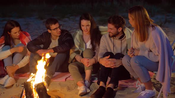 Group of Friends Sitting at Camp Fire on Beach