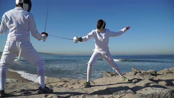 A man and woman fencing on the beach