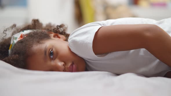 Little Cute African American Girl Lying on Bed and Smiling at Camera