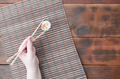 A hand with chopsticks holds a sushi roll on a bamboo straw serwing mat background - PhotoDune Item for Sale