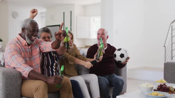 Two diverse senior couples sitting on a couch watching a game drinking beer cheering