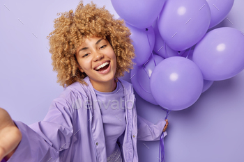 oat holds bunch of inflated balloons celebrates birthday makes selfie photo has festive mood isolated over purple background. Monochrome shot