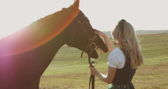 Happy Slavic Girl Has a Fun and Caresses a Brown Horse Among the Wide Meadows