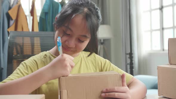 Close Up Of Asian Young Girl Online Seller Writing On Package While Selling Clothes At Home