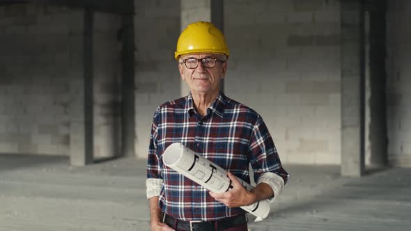 Portrait of caucasian senior engineer holding plans and standing on construction site.