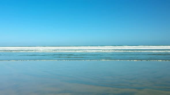 Truck shot of the 90 mile beach, waves breaking in the distance on a sunny day, New Zealand