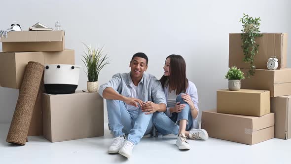 Happy Young Multiracial Couple Caucasian Woman and Hispanic Guy are Sitting on the Floor Between