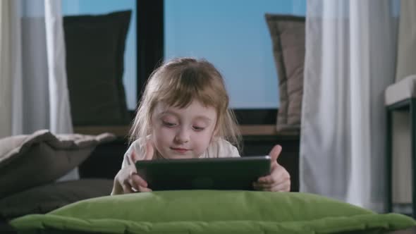 Adorable Kid Girl Using Digital Tablet Watching Cartoons Lying on Bed at Home.