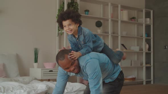 Excited Son Riding on Black Father's Back at Home