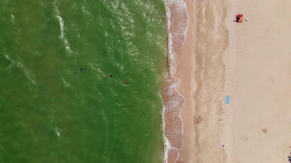 Waves Crashing on Sandy Beach with People Swimming in Sea