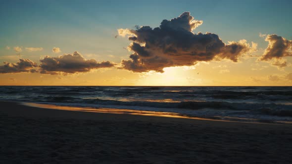 Sunset behind Clouds over Sea Waves and Sandy Beach