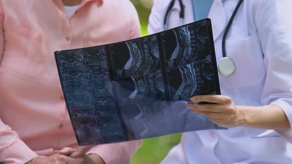 Young Doctor Showing Elderly Patient Joint Examination X-Ray Result, Outdoors