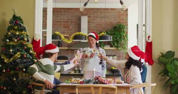 Happy group of diverse friends in santa hats celebrating meal, toasting with vine at christmas time