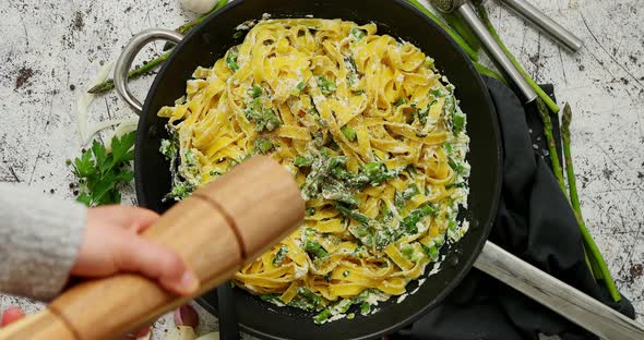 Woman Adding Fresh Pepper To Homemade Tagliatelle Pasta with Ricotta Cheese Sauce and Asparagus