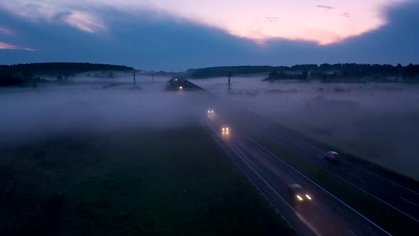 Cars With Their Lights On Drive At Dusk On The Highway Through Fog Aerial View