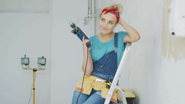 Happy Woman with Drill Sitting on Stepladder