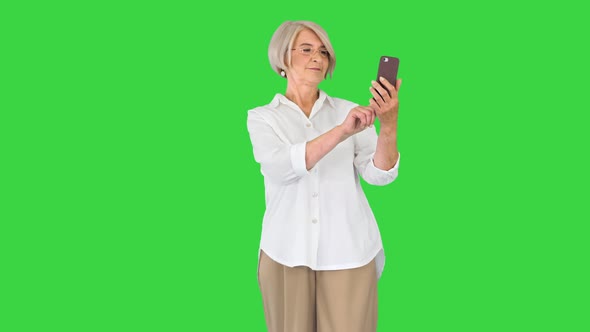 Positive Elderly Woman Smiling and Using Her Smartphone While Making Selfies on a Green Screen