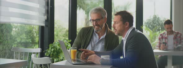 Two smiling men in cafe above laptop