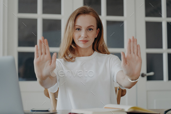 Serious young female showing stop gesture by palms, saying no to gender discrimination on workplace