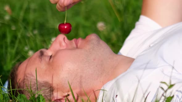 Young Girl Relaxes Lying on the Green Grass and Eats Berries