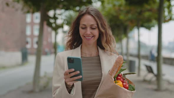 Smiling Woman Using Mobile and Carrying Grocery Bag