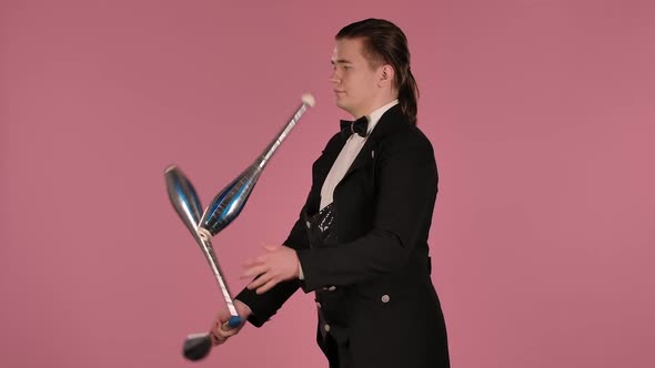 The Juggler Uses Clubs Juggling in the Studio on a Pink Background