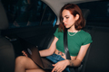 Beautiful woman is using laptop while sitting on back seat - PhotoDune Item for Sale