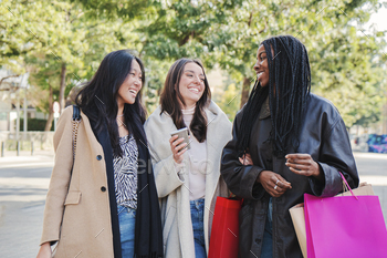 Three multiracial happy young women walking and talking on a shopping day. Group of girls carrying