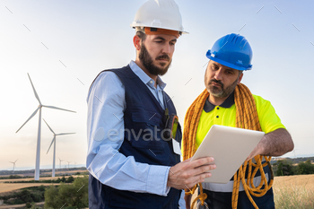 Engineer and wind turbine farm maintenance worker looking together plans in digital tablet.