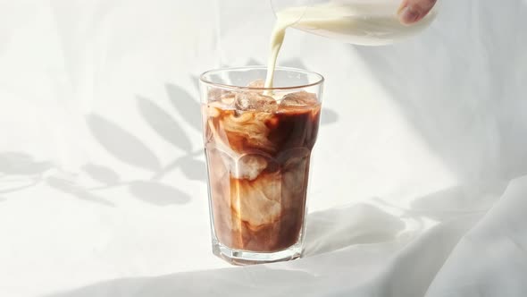 Milk cream is poured into a iced coffee. Coffee cold drink