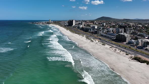 Drone flight over Bloubergstrand shoreline with beachfront buildings in Cape Town, South Africa, at