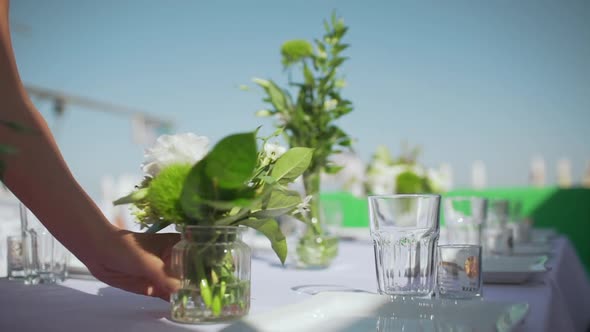 Woman Putting Bouquets in Vases on White Draped Table with Plates Glasses and Cutlery on It