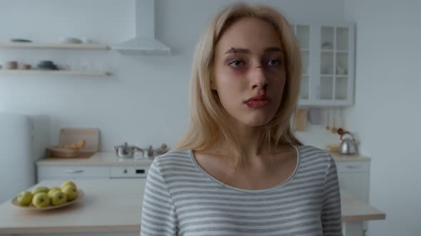 Close Up Portrait of Young Battered Woman with Wounds and Bruises on Face Standing Alone at Kitchen