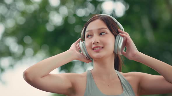 Happy asian woman adjusting wireless headphones before starting jogging