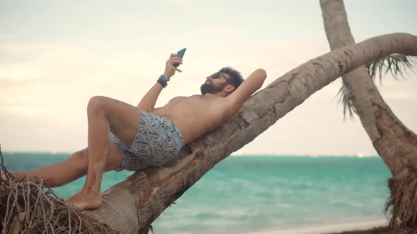 Man Resting On Ocean And Hold Mobile Phone. Man Laying On Palm And Tapping On Smartphone On Vacation