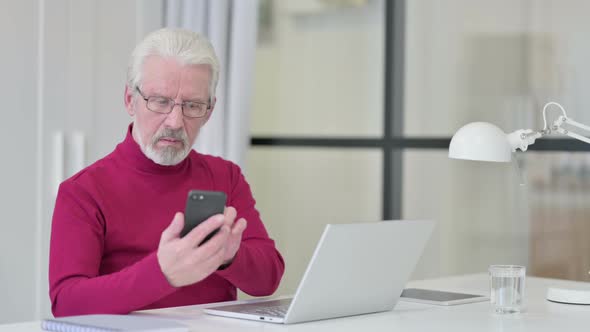 Old Man with Laptop Using Smartphone at Work